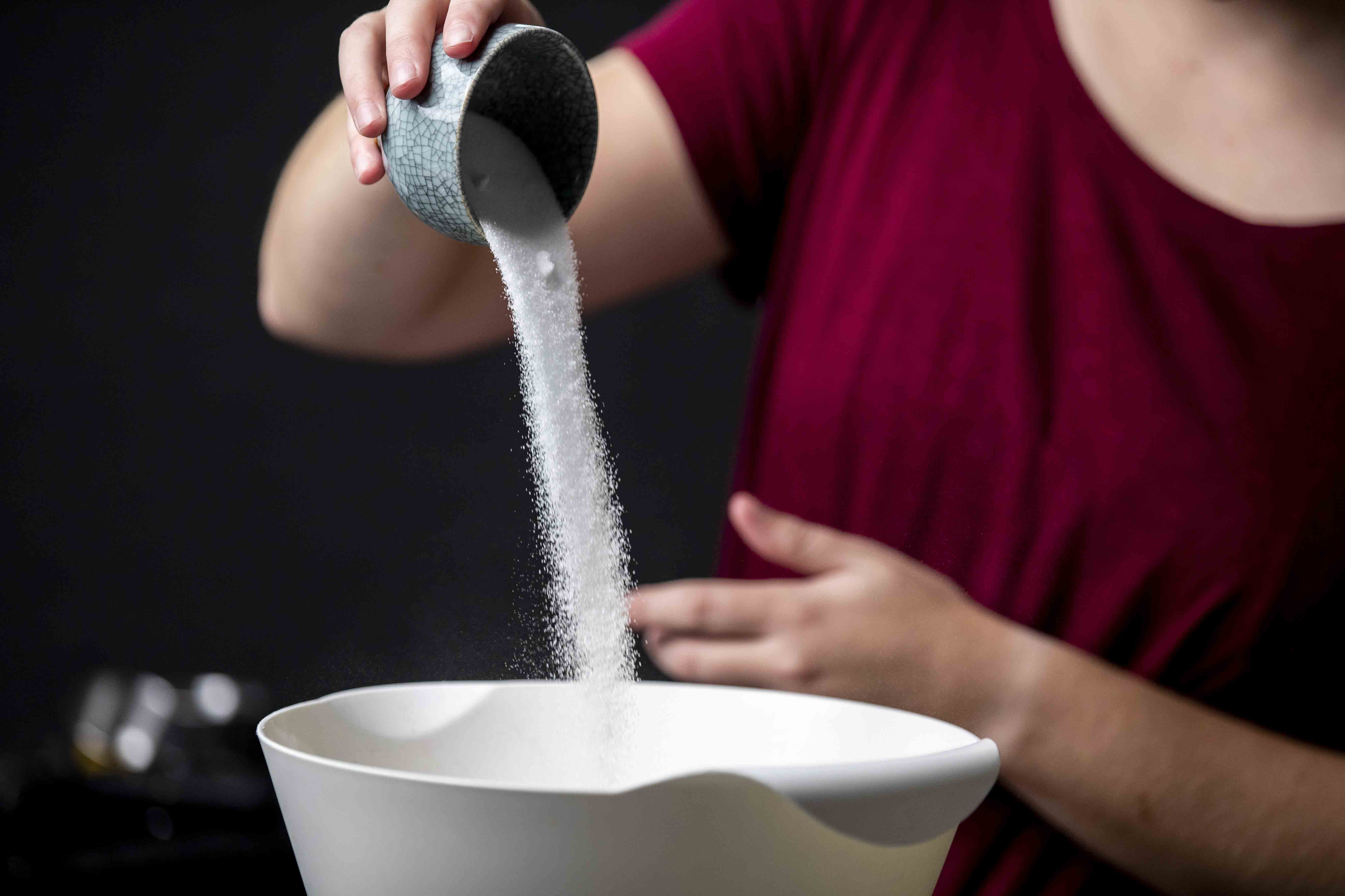 Pouring sugar into a white bowl for the cranberry-pear pie filling.