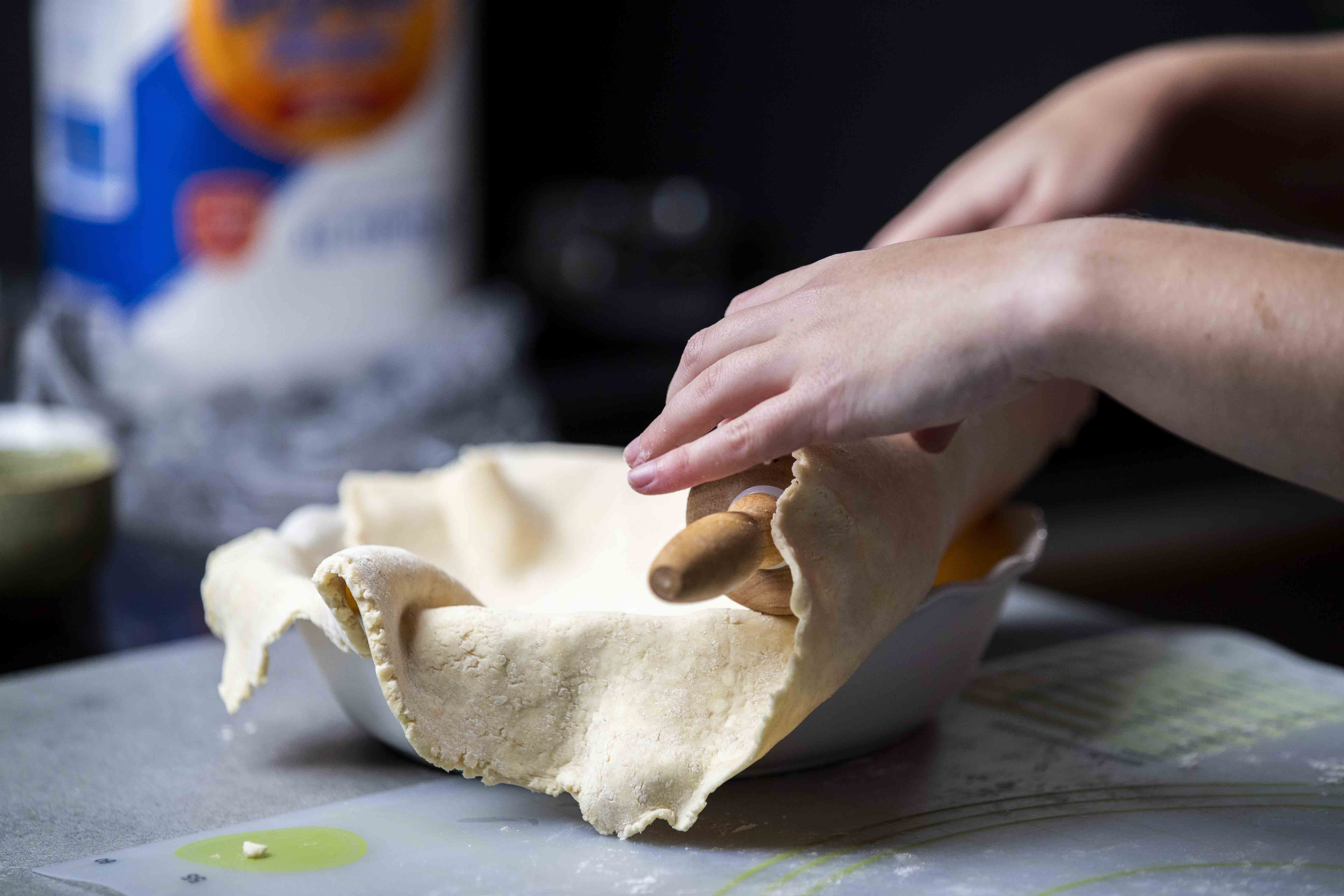 Taking the rolled out pie dough and placing it into a pie pan by folding part of the dough over a rolling pin.