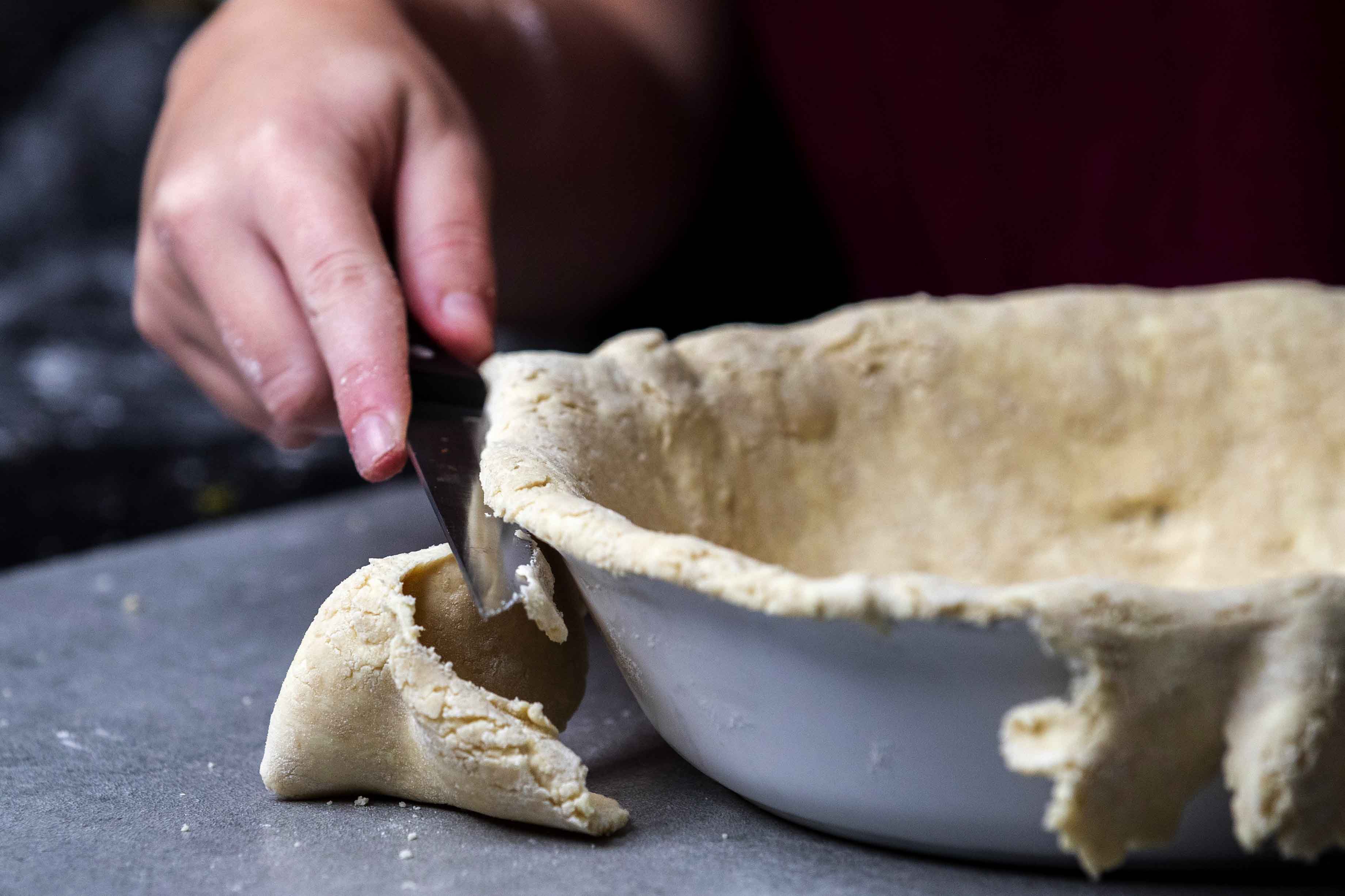 Trimming off dough hanging over the edge of the pan with a knife.