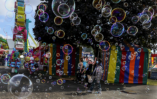 Every year, I enjoy covering fairs large and small, always looking for a different image. As I did a final walk-around before leaving the Washington State Fair in Puyallup, a machine at a vendor's stand was producing hundreds of bubbles. Using this as a curtain to the scene, it needed the dark background provided by the trees. The small Ferris wheel, SpongeBob SquarePants (left) and a person framed by a tent’s opening complete it.