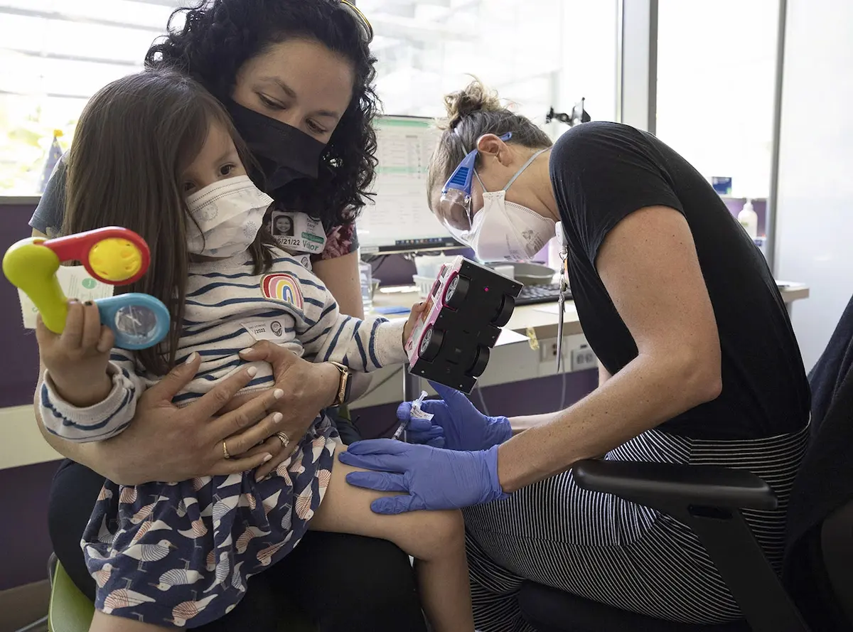 Three-year-old Alba Kerr is held by her mom, Rachel Kerr, while receiving her first dose of a COVID-19 vaccine for children aged 6 months to 4 years from Seattle Children’s Hospital RN Kara Lueneburg. Alba was distracted by toys and didn’t let out a peep.