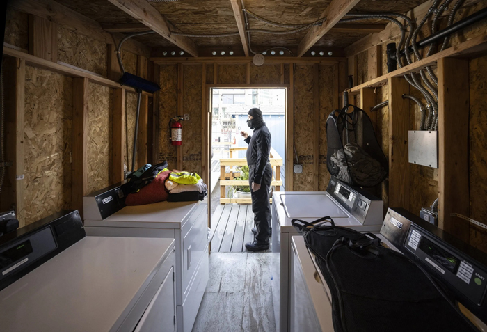 A resident of Rosie's Place Tiny House Village stands at the entry way of the laundry facility. He goes by the name of Grand Master Shadow, is 27, and has been homeless on and off since 2013. (Steve Ringman / The Seattle Times)